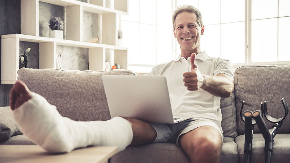 Mand med brækket i ben i gips, der sidder med laptop.